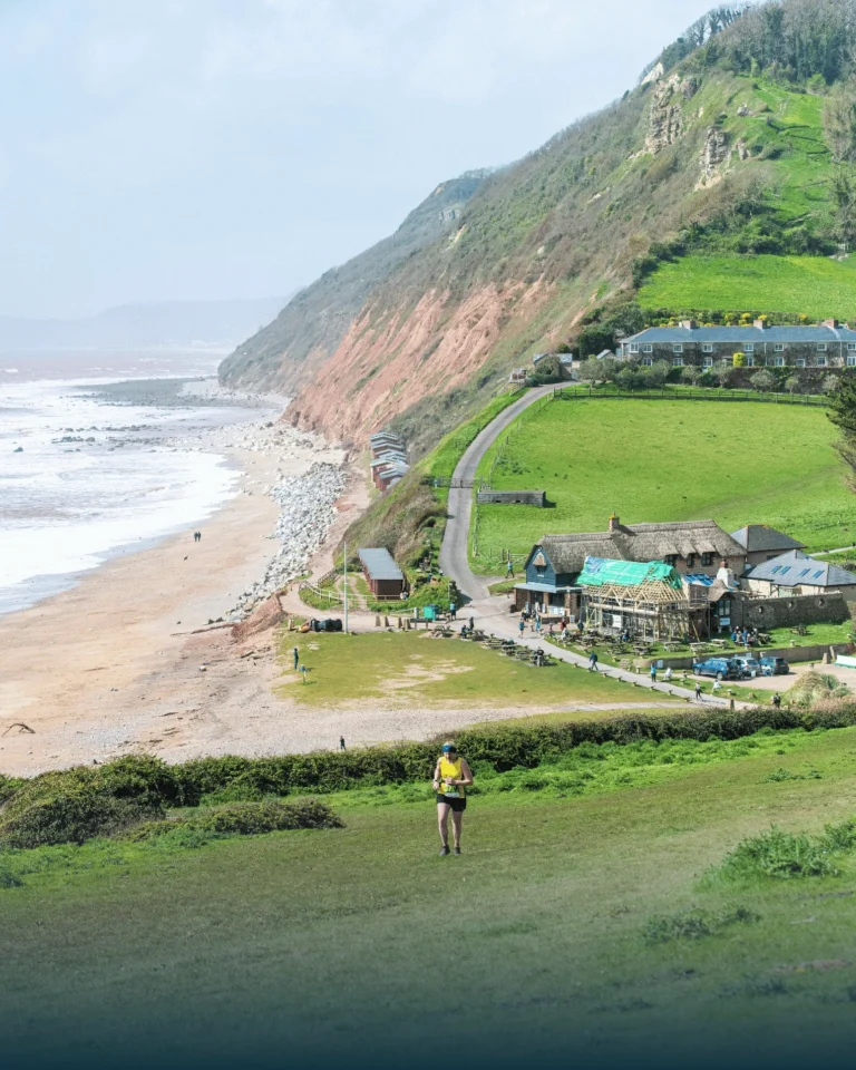 Trail runner taking on the Exe to Axe, descending a coastal hill above Branscombe beach